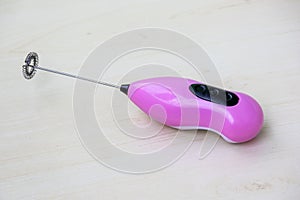 Pink electric milk frother on wooden background. Portable mini electric beater. photo