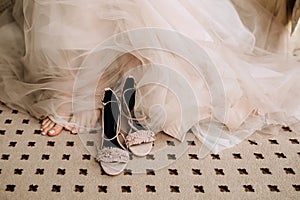 Pink elegant shoes of the bride`s sandals on the floor next to the feet and a wedding gentle dress made of translucent