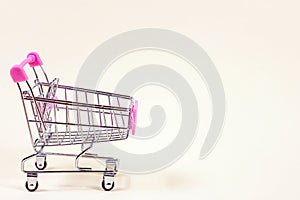 Pink empty shopping cart from the supermarket as a symbol of consumption and consumerism on light background with copy space