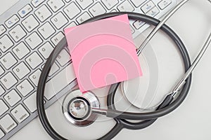 Pink empty sticky post note paper sheet on computer keyboard with stethoscope. heart and healthcare concept. diagnostic, disease,