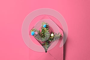 Pink envelope with fir tree branches and baubles on pink background