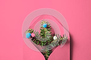 Pink envelope with fir tree branches and baubles on pink background