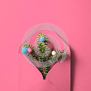 Pink envelope with fir tree branches and baubles on pink background