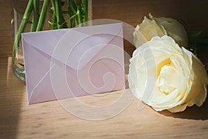 Pink envelope letter and white rose flower on wood table with sunlight