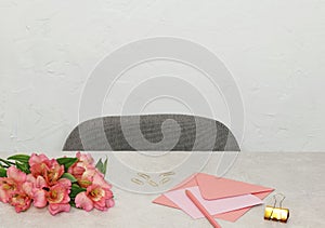 Pink envelope with paper blank, flowers and office accessories on stone desk