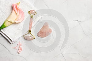 A pink facial massage , a face roller Gua Sha with pink flowers over the marble background.