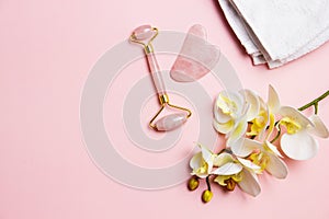 A pink facial massage , a face roller Gua Sha with pink flowers over the pink background.