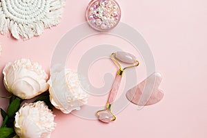 A pink facial massage , a face roller Gua Sha with pink roses over the pink background.