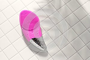 Pink facial sonic brush for massage on white tile with water drops