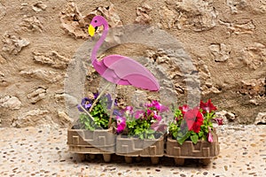 Pink flamingo sitting in a flower pot with petunia flowers on \