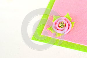 Pink flower with green leaf on a color felt and white wooden background