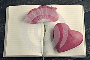 Pink flower of poppy on an open notebook and one decorative hearts.