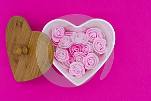 Pink flowers in a heart-shaped casket with wooden lid against a pink background. Valentines day background.