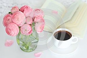Pink flowers in vase, cup of coffee and open book on the table.
