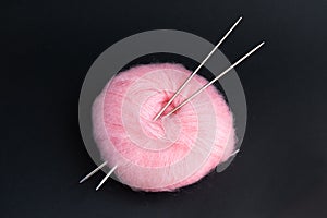 Pink fluffy yarn ball with knitting needles on black background.