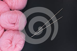 Pink fluffy yarn balls and two metal knitting needles on a black background.