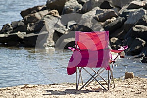 A pink foldable camping chair on a rocky beach