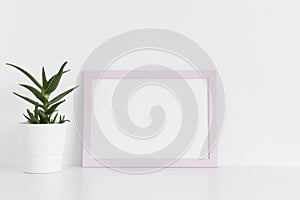 Pink frame mockup with a aloe vera in a pot on a white table.Landscape orientation