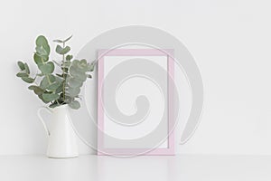 Pink frame mockup with a bouquet of eucalyptus in a vase on a white table.Portrait orientation