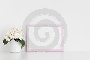 Pink frame mockup with a hortensia in a pot on a white table.Landscape orientation