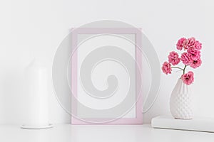 Pink frame mockup with pink roses in a vase and candle on a white table.Portrait orientation