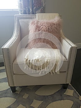 Pink furry throw pillow and soft white blanket on armchair inside a bedroom