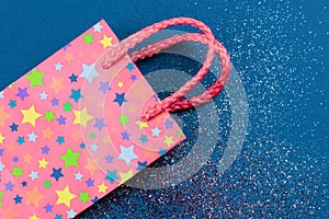 Pink gift bag on abstract red, white and blue glitter sparkle background. Holiday concept. Flat lay.