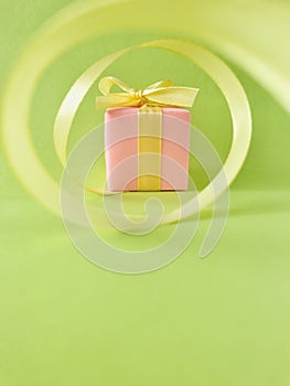 Pink Gift box at the end of the spiral yellow ribbon, green background, vertical.