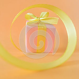 Pink Gift box at the end of the spiral yellow ribbon, orange background. square.