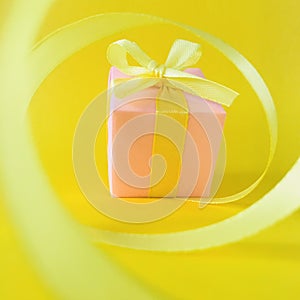 Pink gift box at the end of the spiral yellow ribbon, yellow background, blurs.