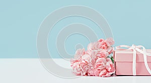 Pink gift box with pink carnations nearby on table