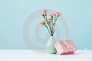 Pink gift box with pink carnations in vase on table