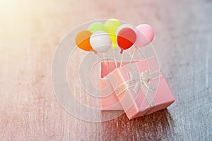 Pink gift box with silver ribbon and colorful balloon on wooden background. minimal hollyday concept