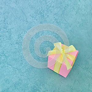 Pink gift box on teal green background. Square photo image.