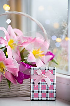 Pink gift box and tender bouquet of beautiful pink tulips in white basket near window with raindrops in the daylight