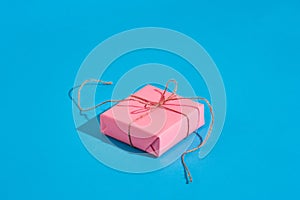 Pink gift box with thin tied rope with shadow on blue background