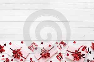 Pink gift boxes with red ribbons and bows, confetti hearts on a white background. Copy space Flat lay. Greeting card for