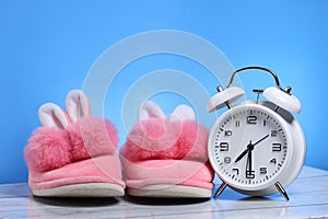 Pink girl slippers with white retro alarm clock on a wooden floor and blue background