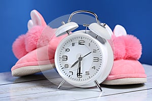 Pink girl slippers with white retro alarm clock on a wooden floor and blue background