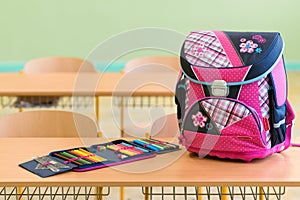 Pink girly school bag and pencil case on a desk in an empty classroom. First day of school.