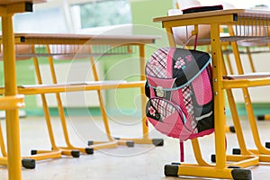 Pink girly school bag and pencil case on a desk in an empty classroom. First day of school.