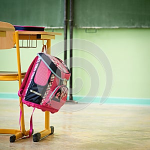 Pink girly school bag and pencil case on a desk in an empty classroom. First day of school.