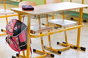 Pink girly school bag and pencil case on a desk in an empty classroom. First day of school.