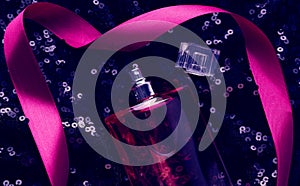 Pink glass bottle with pink perfume liquid on black background with shiny sequins