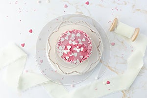 Pink glazed cupcake on retro plate with heart shape sprinkles on white golden marble table background