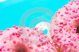 Pink glazed doughnuts with sugar sprinkles on white cake stand with hearts, light blue background, copyspace, birthday, card, post