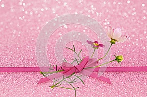 Pink glitter background with ribbon bow and cosmos flowers