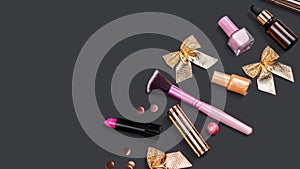 Pink and gold makeup accessories on black background with confetti and bows. Lipstick, nail Polish. Cosmetic. Xmas gift.