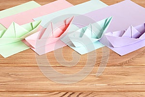 Pink, green, lilac, blue paper origami ships toys on wooden table with empty space for text. Colored paper sheets