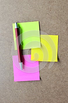 Pink, green, yellow note paper and red pen on wooden background.